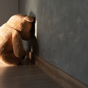 Teddy bear sitting alone with its head lowered against a wall